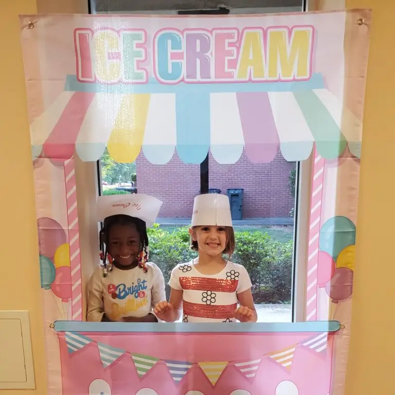 A black girl and a white girl pose together in temporary ice cream booth with hats on