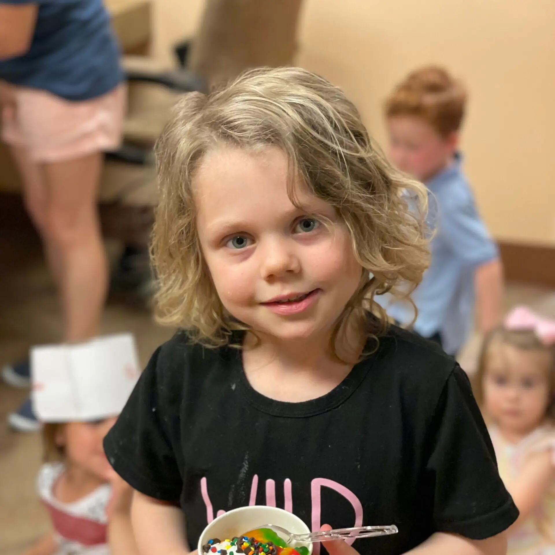 Little girls with wavy light brown hair in black shirt holding a bowl of ice cream