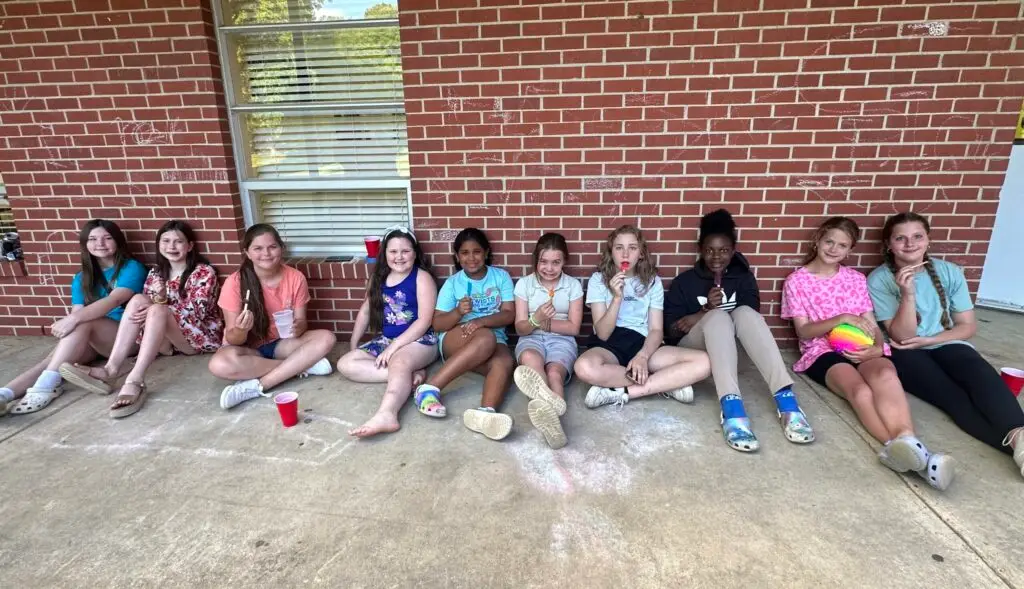 Girls sit on sidewalk along a brick wall