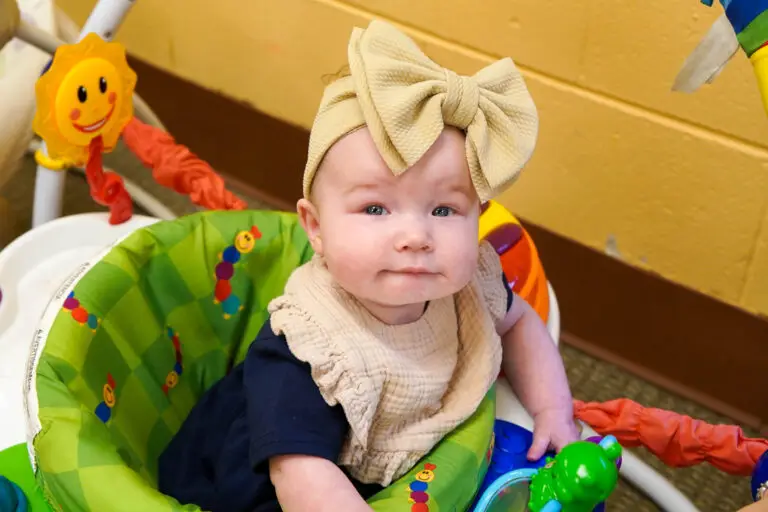 Baby girl sitting in activity seat with big bow on her head