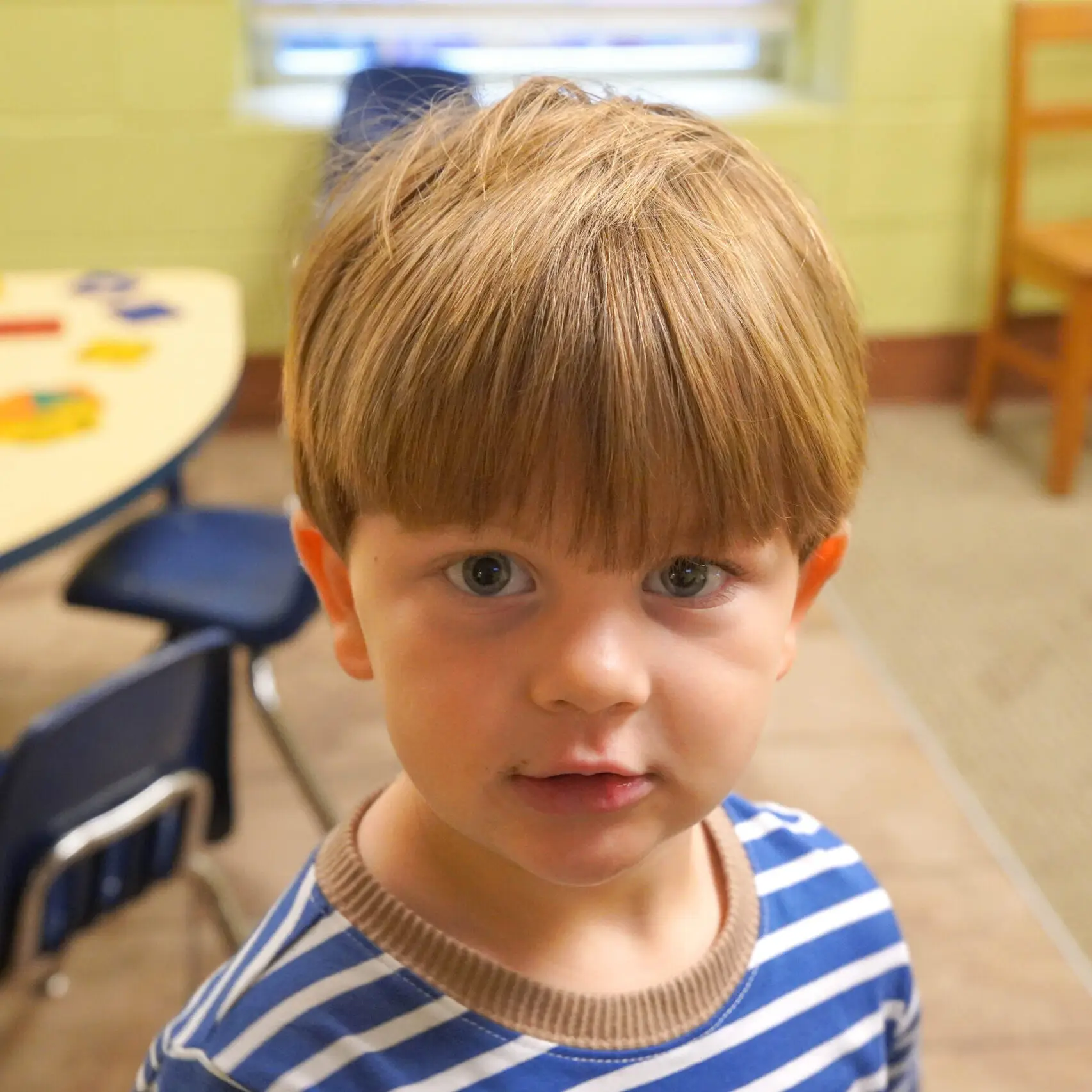 Little boy with dark blonde hair and blue and white striped shirt