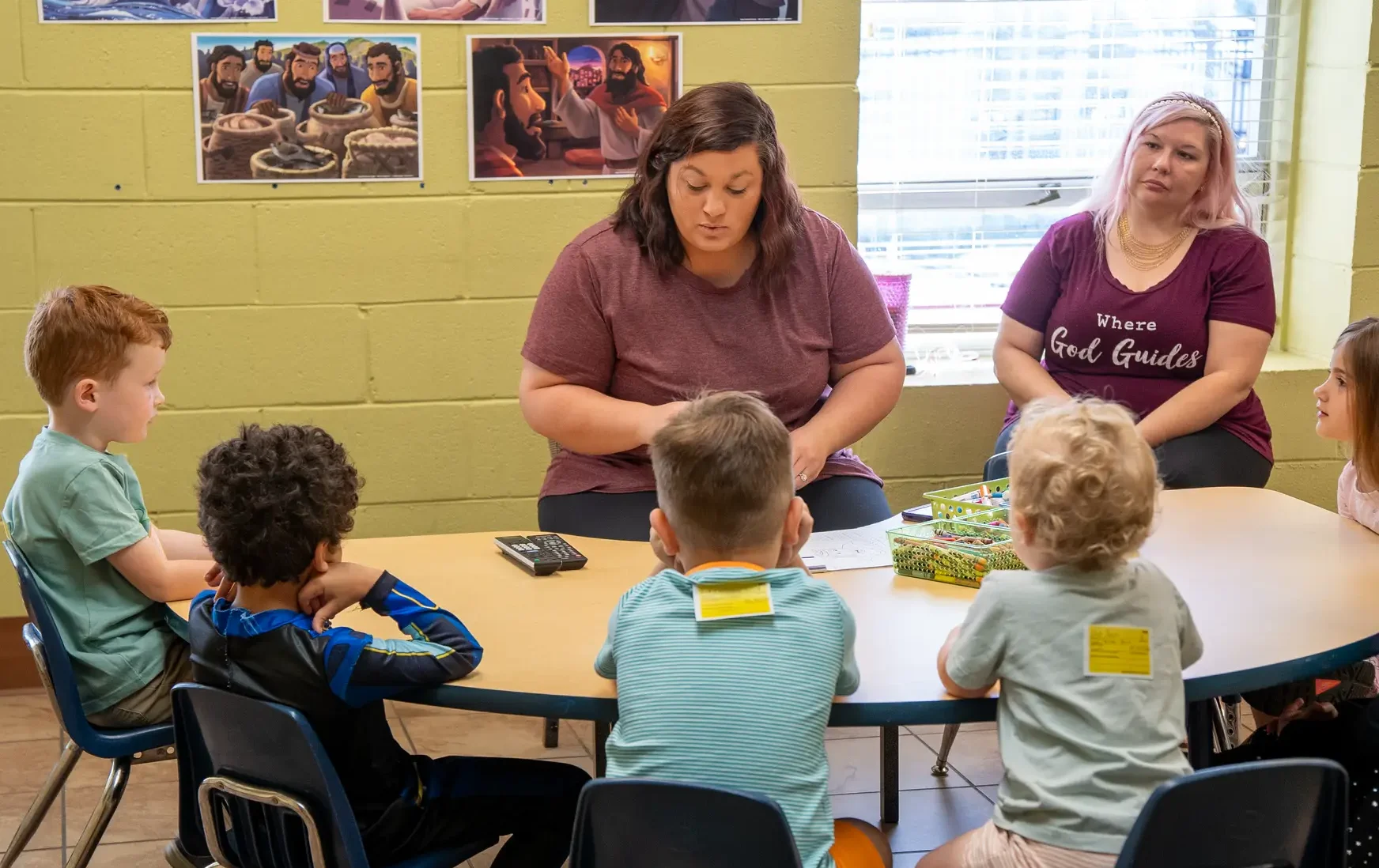 Preschoolers sit at kidney shaped table in front of their Sunday School teacher