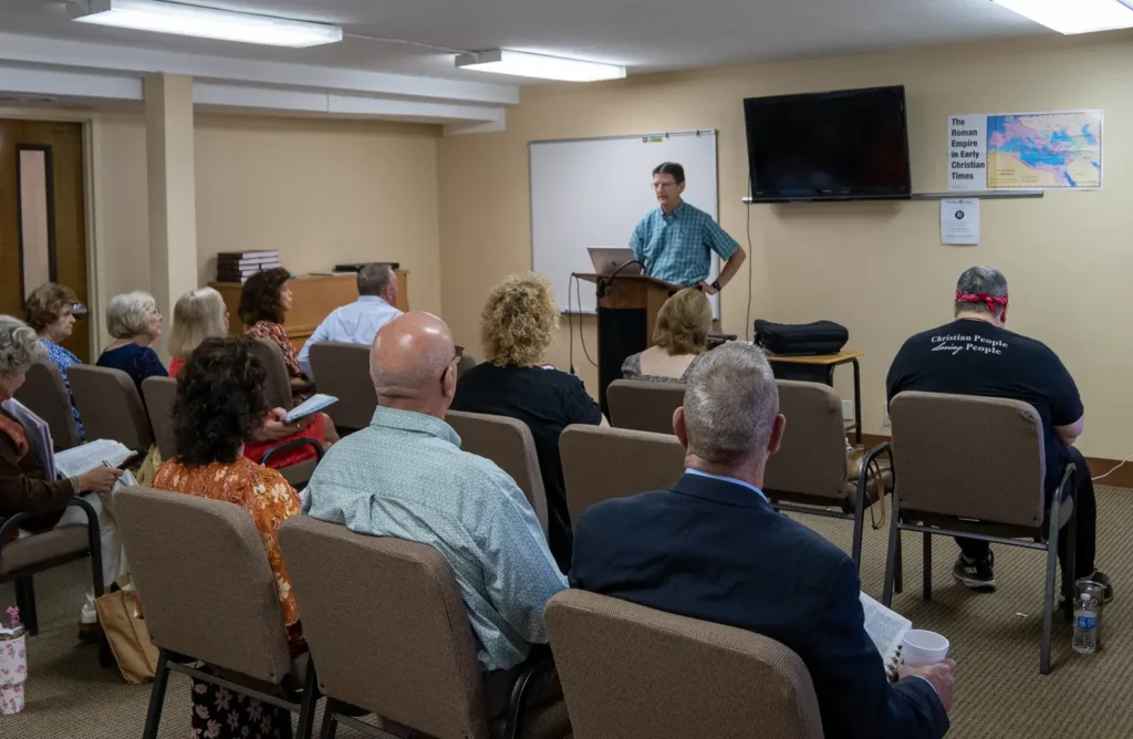 Group of adults sit in Sunday School class with teacher standing at the front of the room