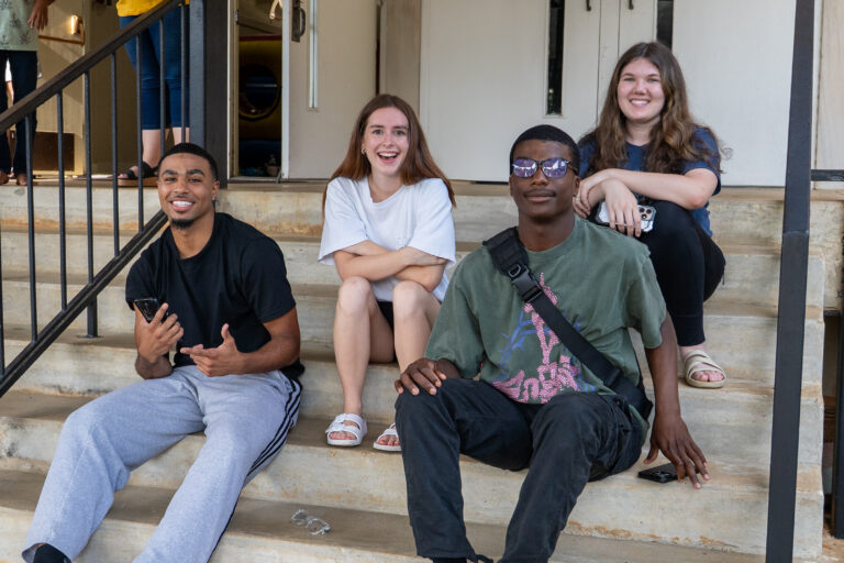 Two college aged girls and two college aged guys sit on cement steps smiling